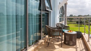 Ein Balkon mit Korbstühlen, einem kleinen runden Tisch und Blick auf eine grüne Landschaft.