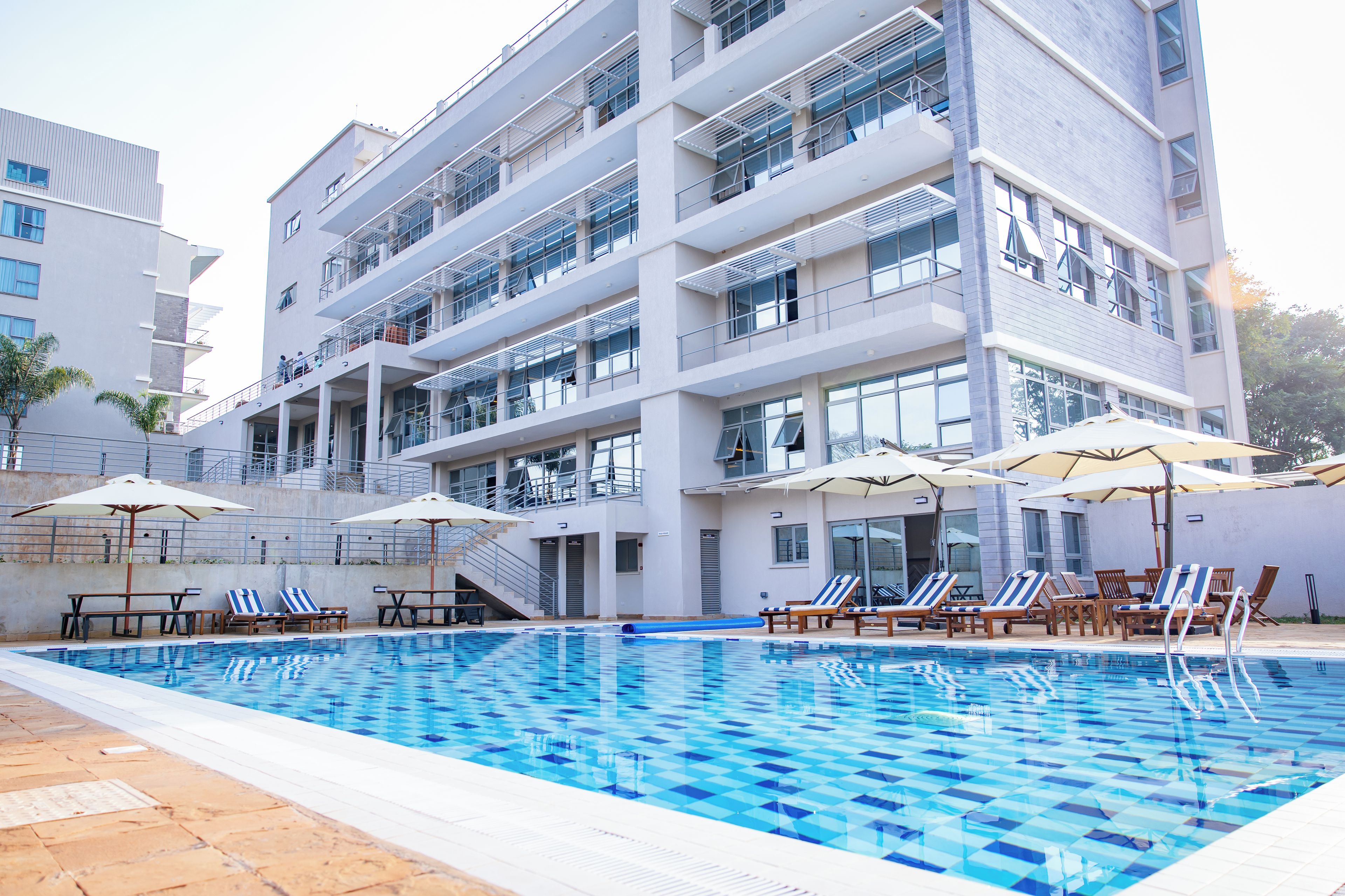 En moderne bygning med swimmingpool, flere balkoner og udendørs siddepladser.
