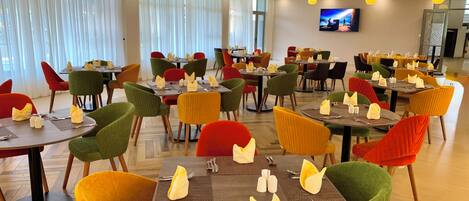 A dining area with multiple tables and chairs, each set with cutlery and napkins.