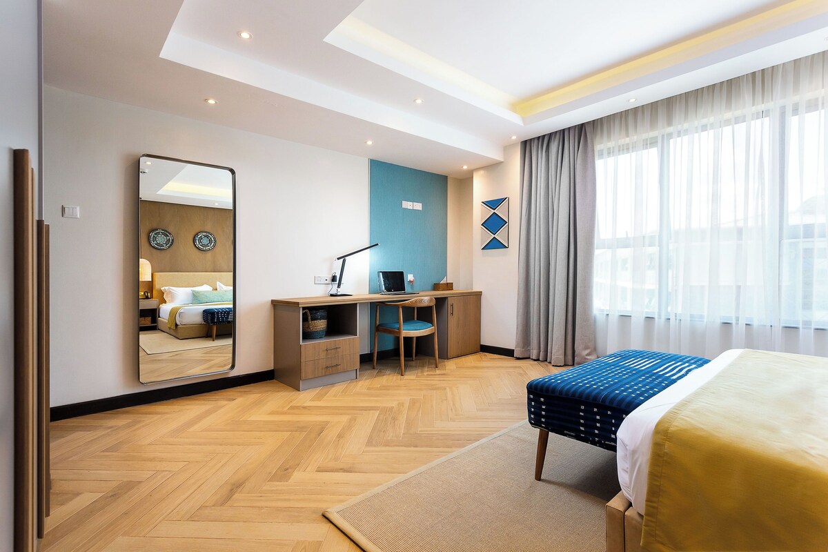 A hotel room with a bed, desk, chair, and a large mirror.