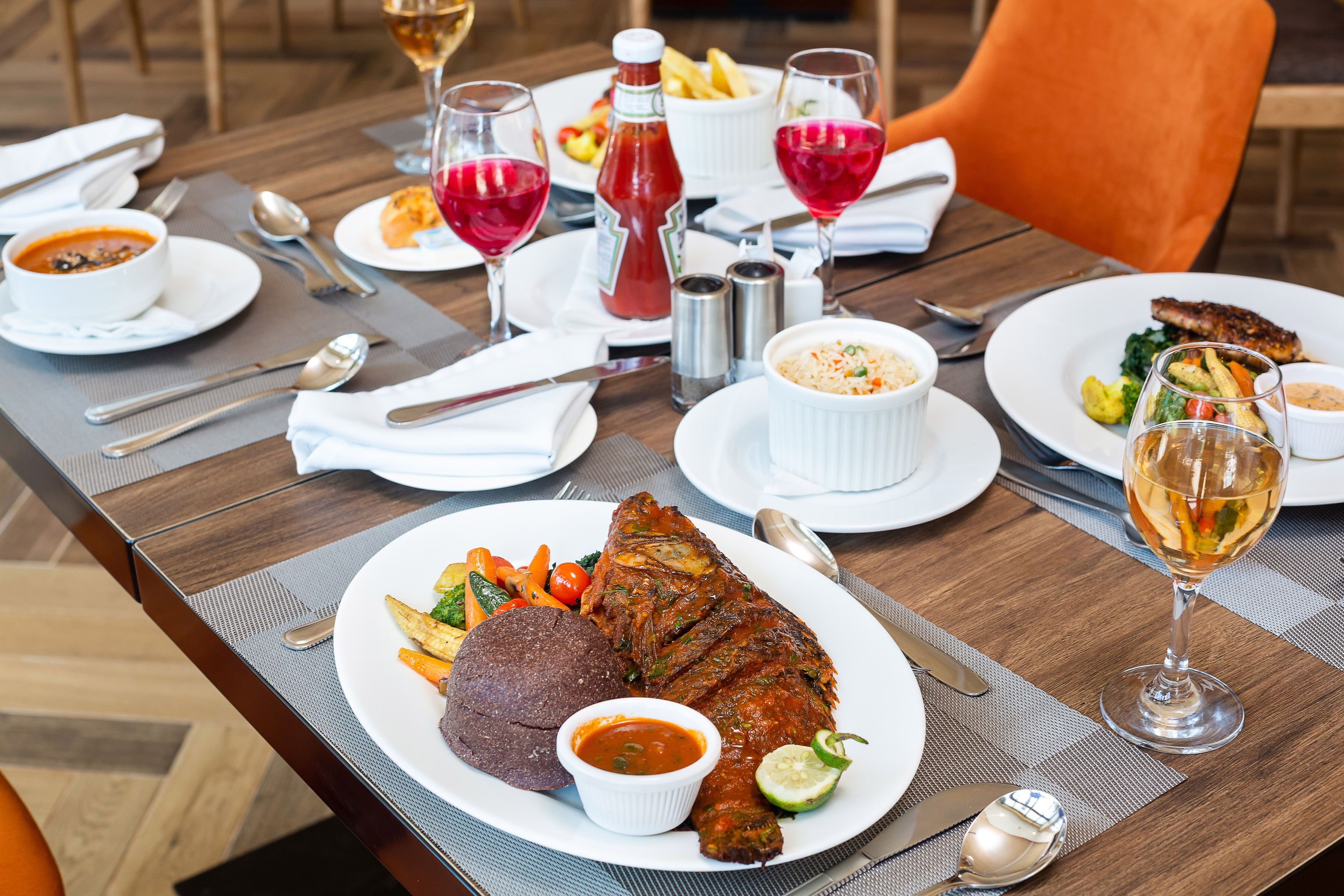 A dining table with a variety of dishes, including a whole fish, vegetables, and a bowl of soup.