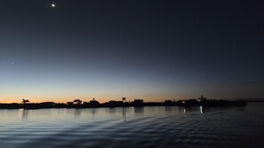 A calm body of water reflecting the sky at dusk with silhouettes of buildings and a boat. - Uros Quechua Lodge (Puno)
