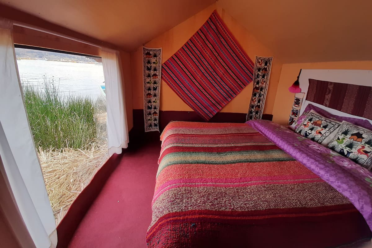 Ein Schlafzimmer mit einem großen Bett, Blick auf ein Gewässer sowie ein Fenster mit Blick auf Gras und Schilf.