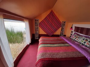 A bedroom with a large bed, a view of a body of water, and a window with a view of grass and reeds. - Uros Quechua Lodge (Puno)