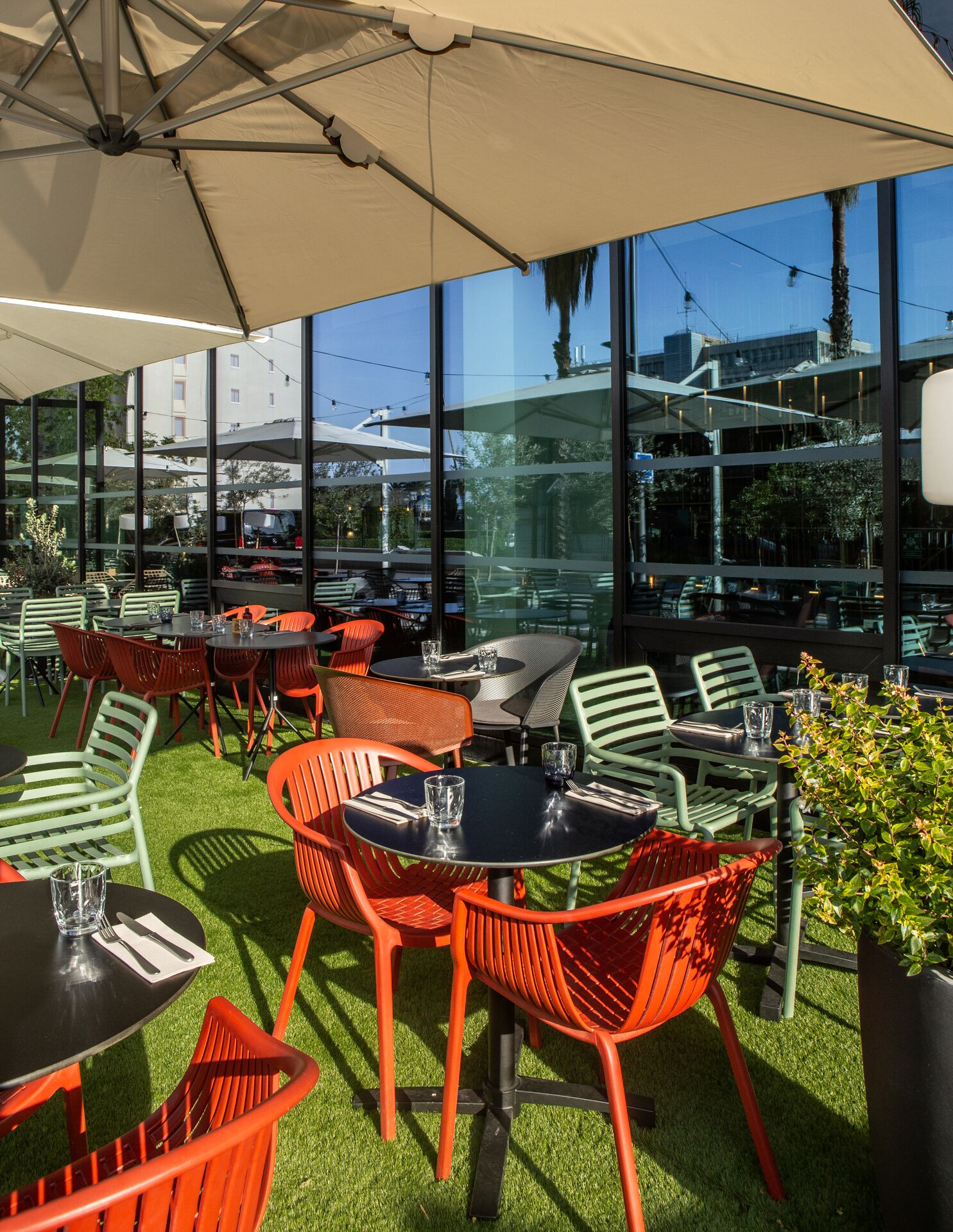 Un espace extérieur aménagé avec des tables et des chaises, de grandes fenêtres et une vue sur le paysage urbain.
