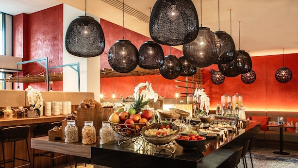 Un espace bar moderne doté d’un long comptoir, d’une variété de plats et de boissons, et de luminaires sphériques suspendus.