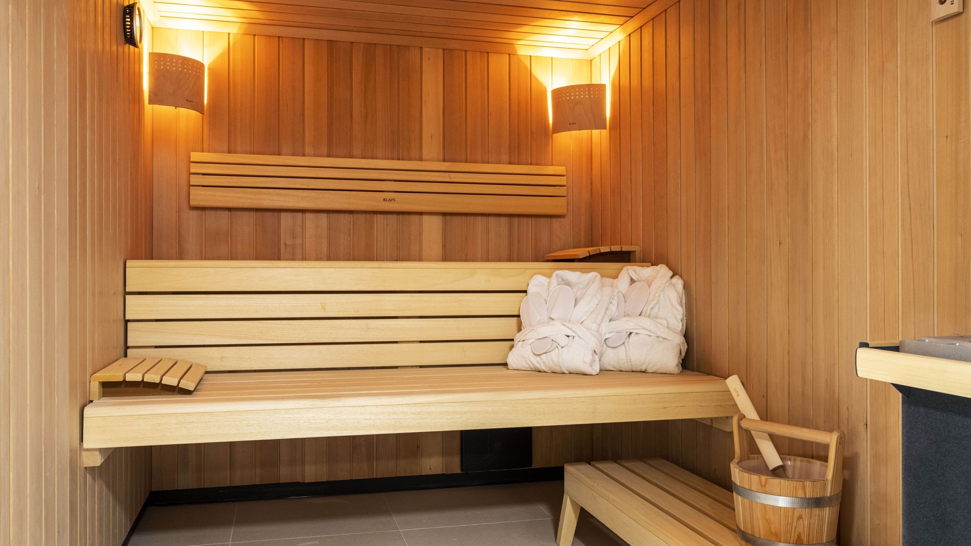 Un banc en bois pour sauna, avec des serviettes et un seau en bois.