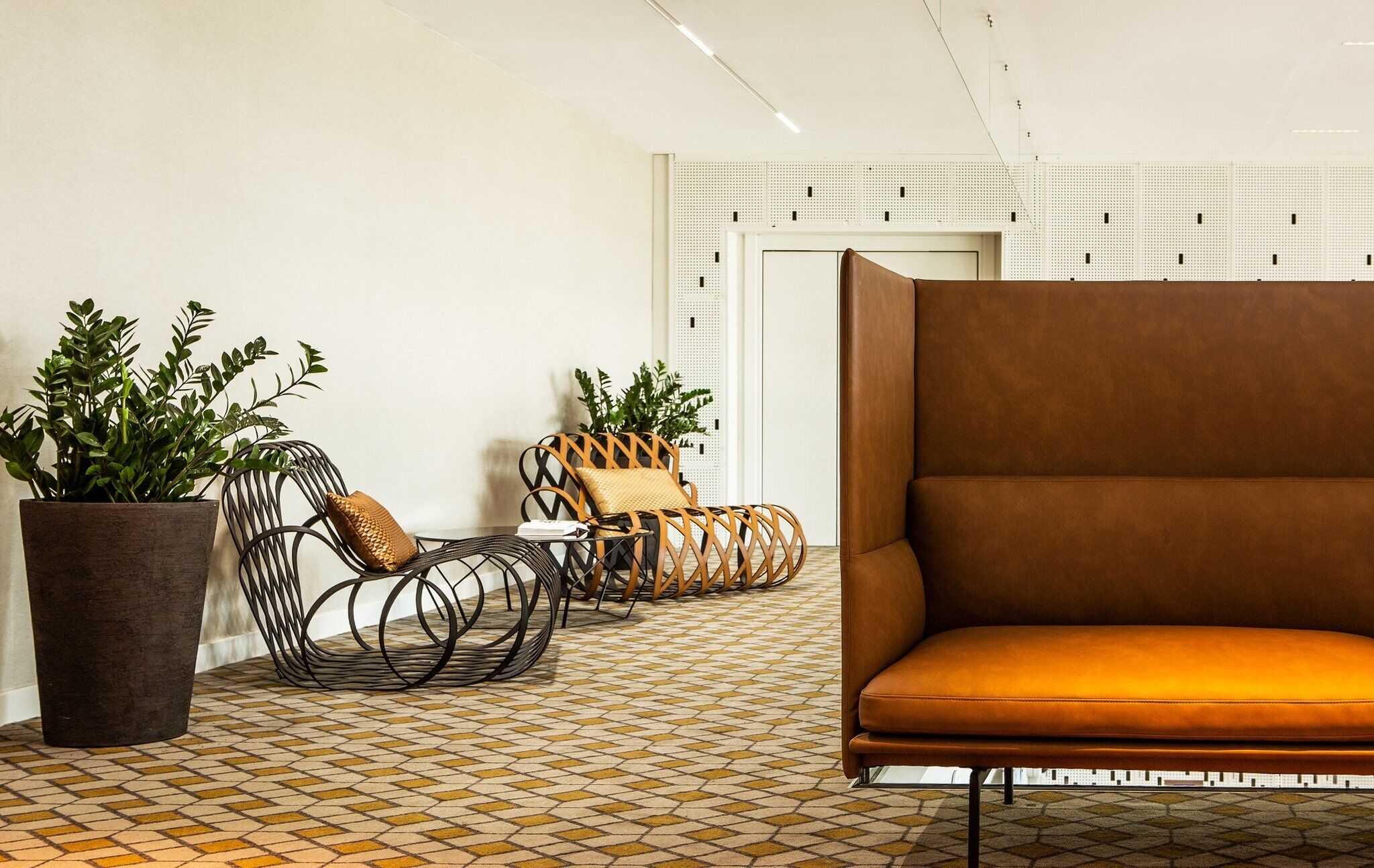 A modern lounge area with a brown sofa, wicker chairs, and potted plants.