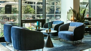 Un espace de détente intérieur moderne, avec des chaises rembourrées bleues, une table ronde et une grande fenêtre donnant sur le paysage urbain.