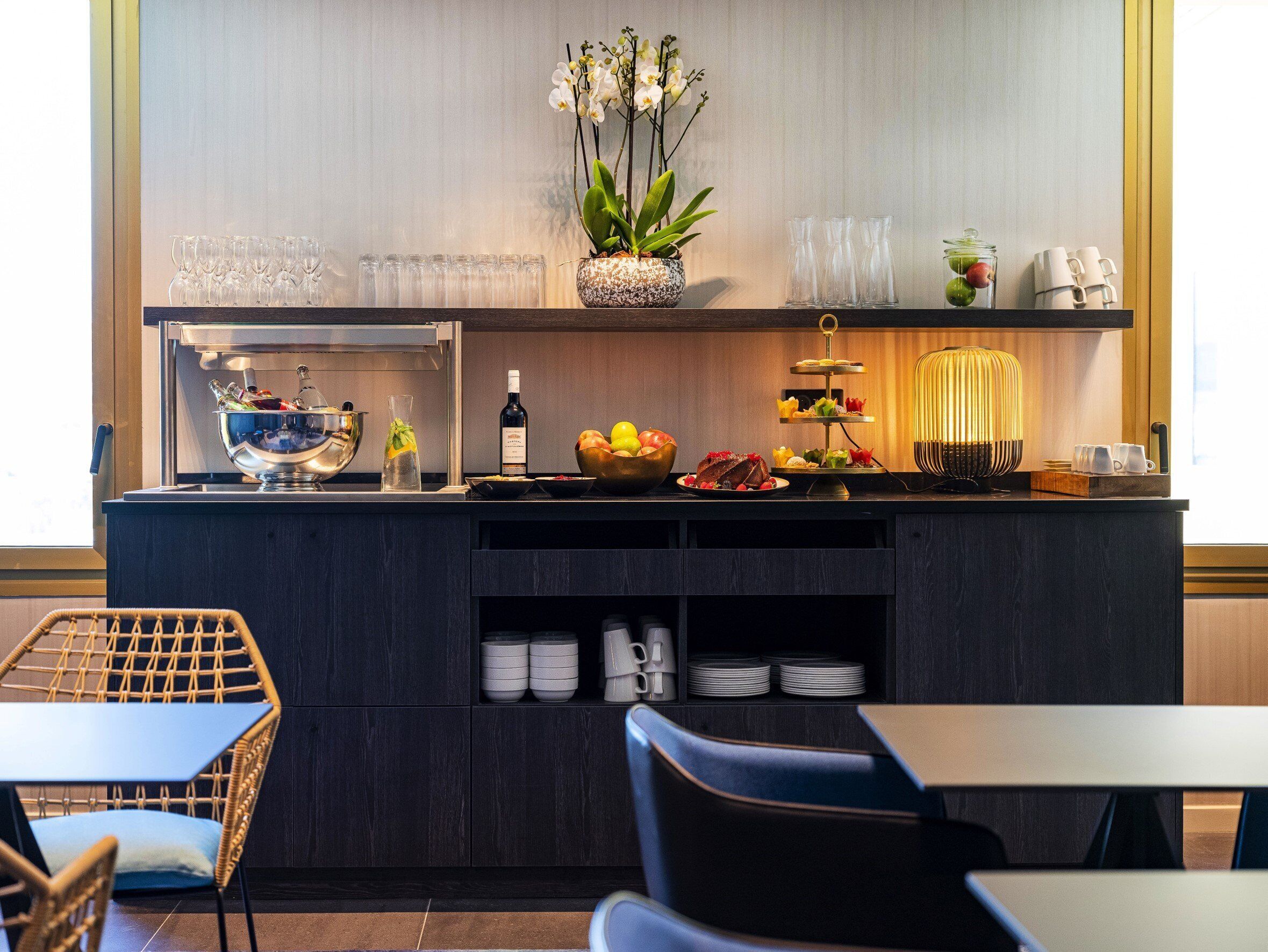 Una zona de bar moderna con una barra de madera oscura, un bol de vidrio, una botella de vino y una bandeja escalonada de aperitivos.