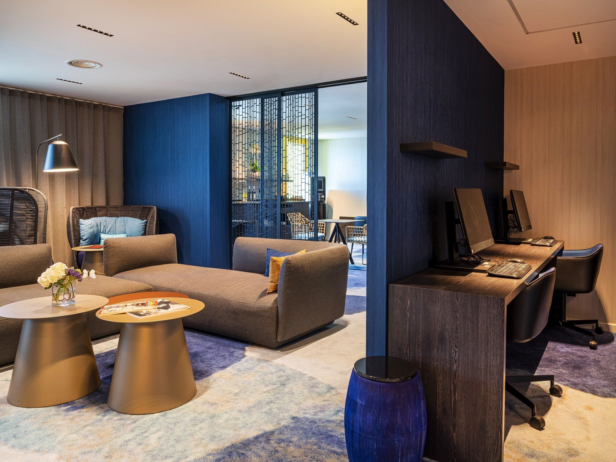 A modern hotel lobby with a seating area, a reception desk, and a large window.