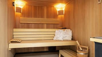 Un banco de sauna de madera con toallas, un cubo de madera y dos apliques de luz en la pared.