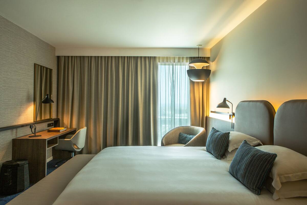 Hotellihuone, jossa on suuri sänky, työpöytä, tuoli ja pöytälamppu.