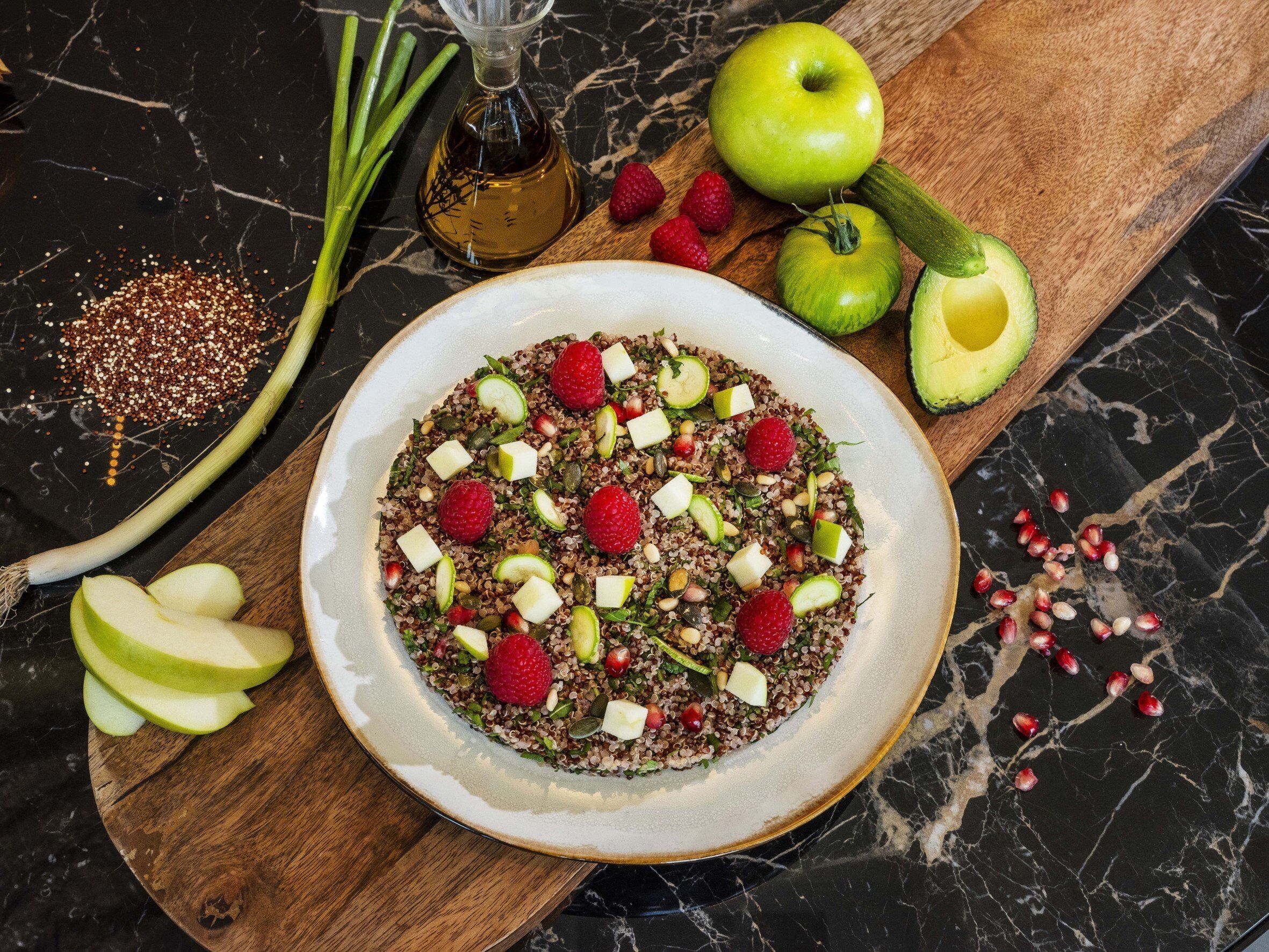 Un bol de salade de quinoa aux fraises et à l’avocat, posé sur une surface en marbre.