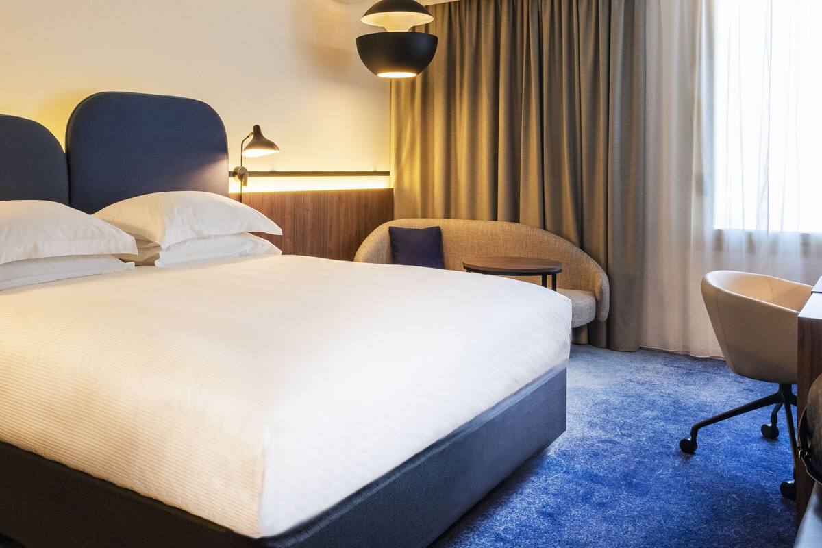 Hotellihuone, jossa on suuri sänky, työpöytä, tuoli ja lamppu.