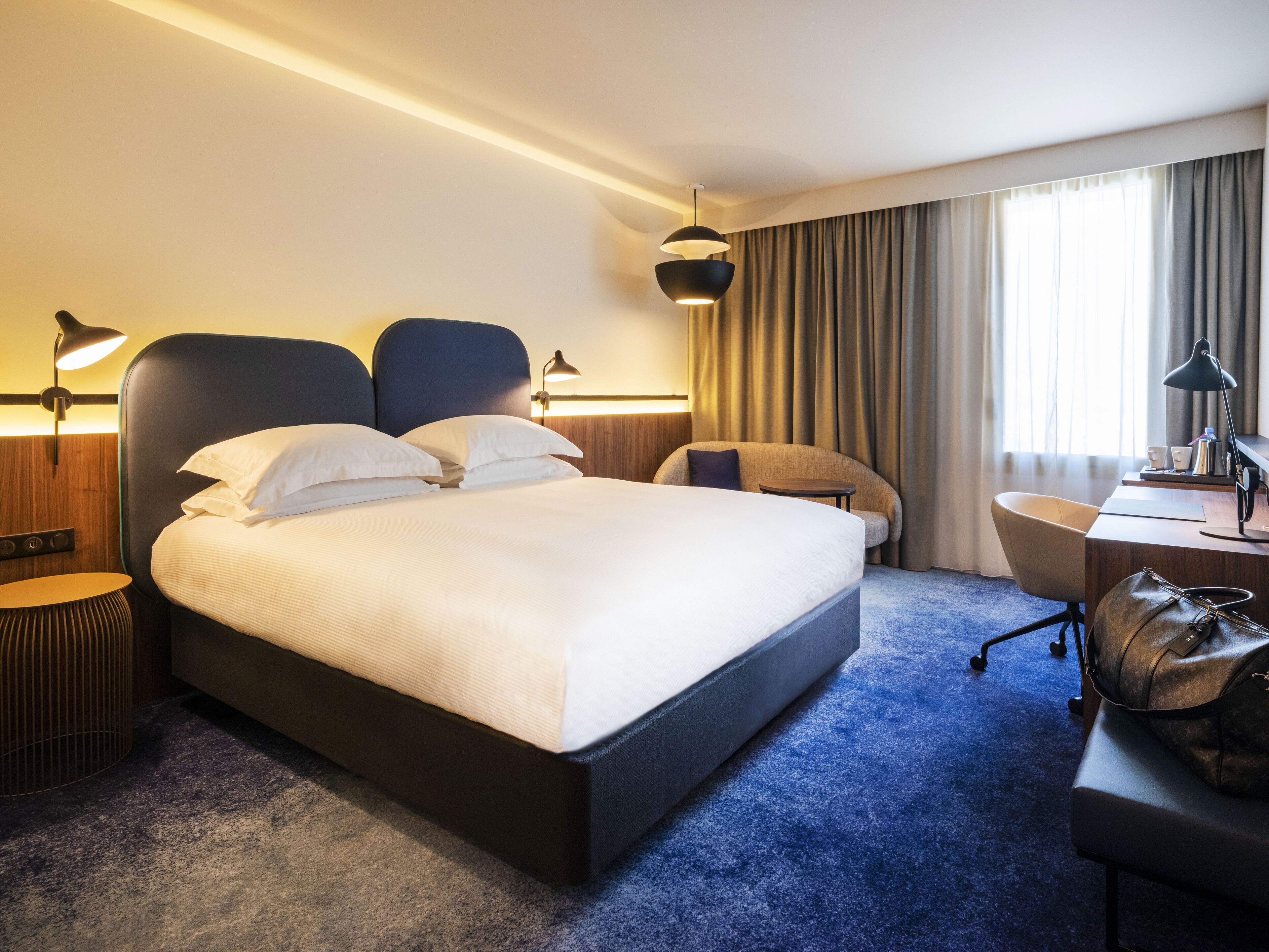 A hotel room with a large bed, a desk, a chair, and a lamp.