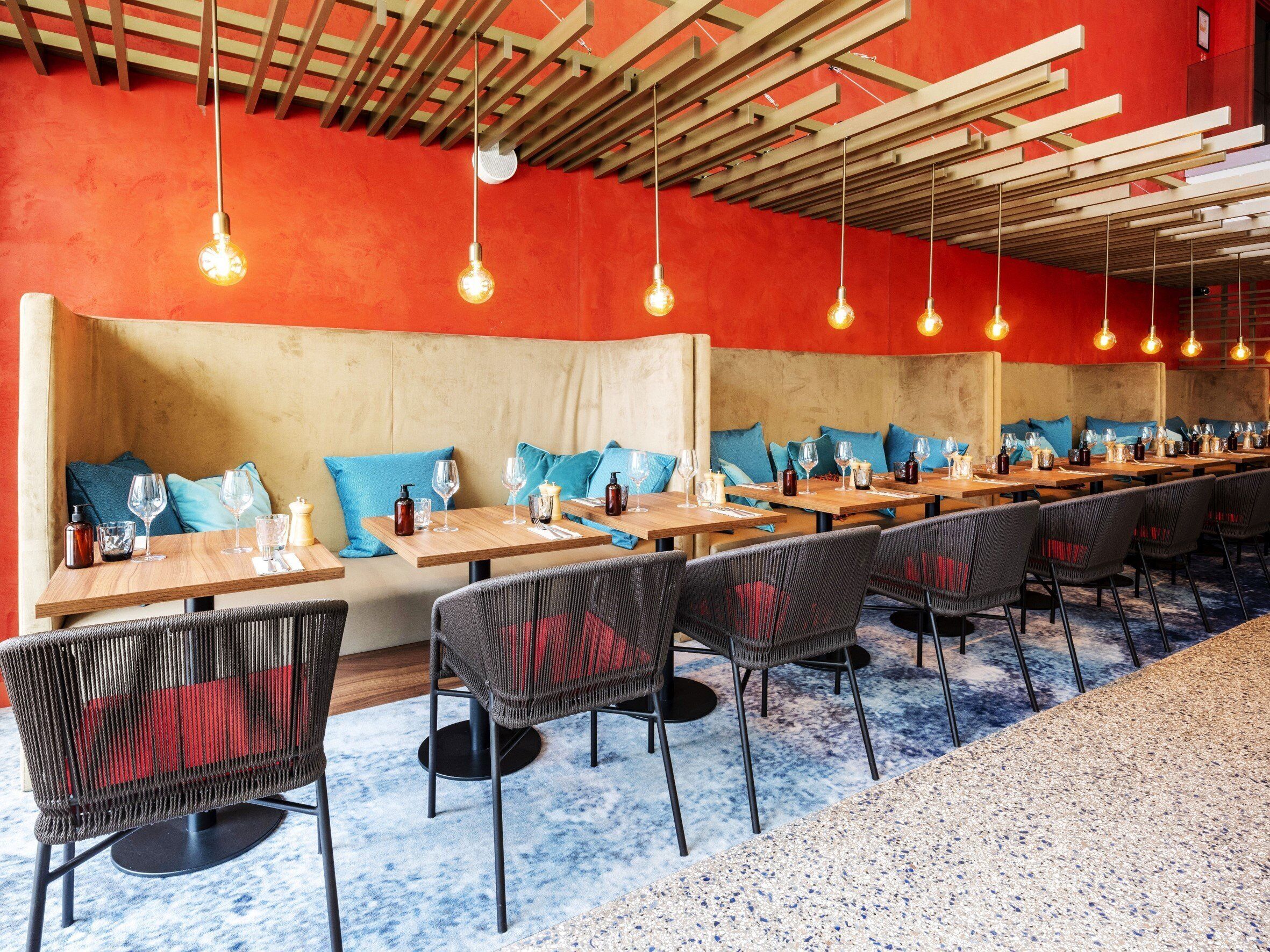Un restaurant avec de longues tables en bois, des sièges rembourrés de tissu bleu et des lampes suspendues.