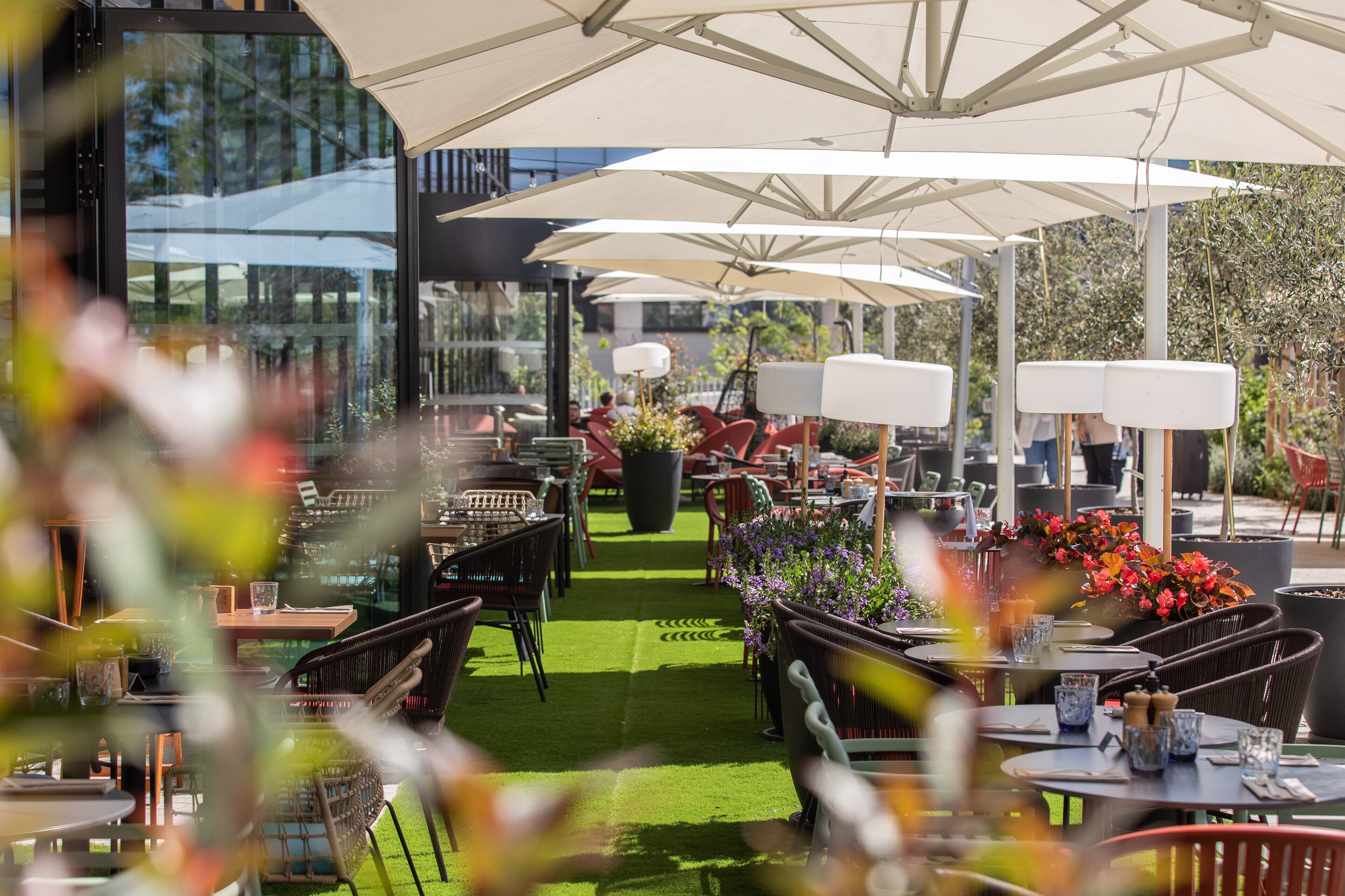 An outdoor seating area with tables and chairs, umbrellas, and potted plants.