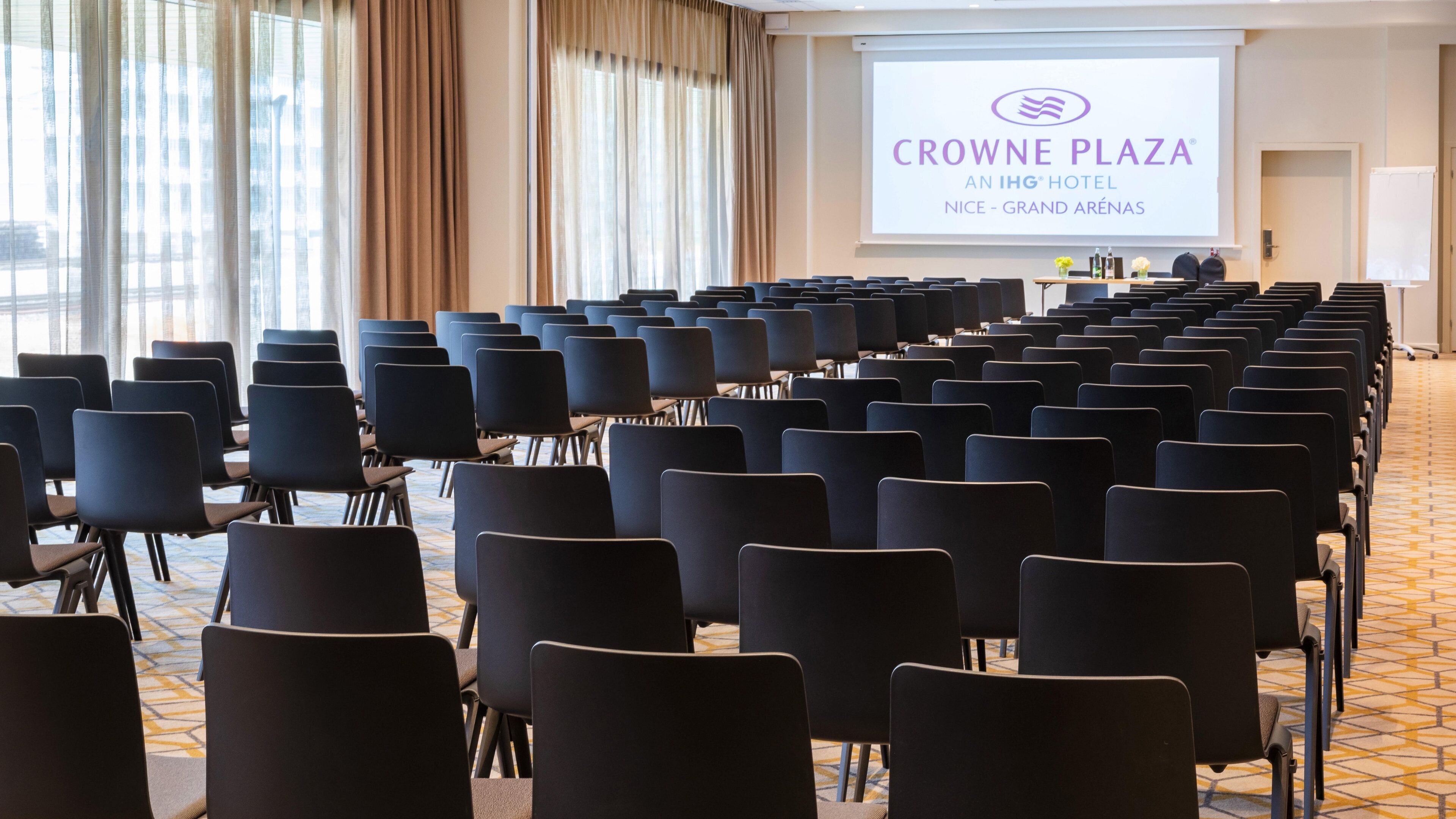 A conference room with rows of chairs facing a projection screen displaying the Crowne Plaza logo.