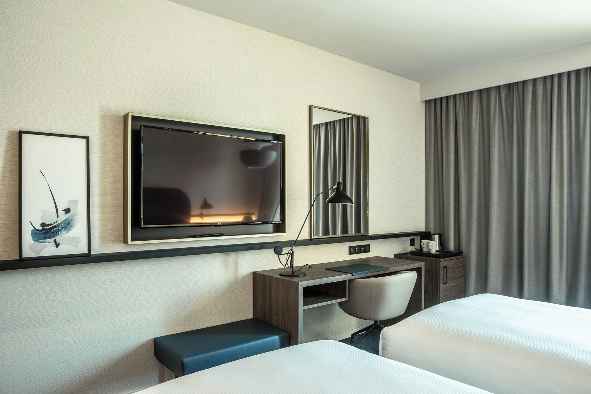 A hotel room with a bed, a desk, a chair, a TV, a lamp, and a window with curtains.