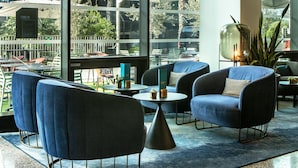 Un espace de détente moderne avec des fauteuils bleus, de petites tables rondes et une grande fenêtre donnant sur l’extérieur.