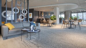 Moderni hotellin aula, jossa on harmaa sohva, pyöreitä pöytiä ja baarialue.