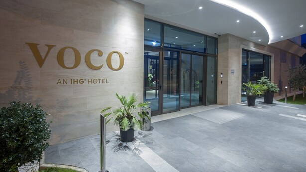 Hotellin sisäänkäynti, jossa on kyltti, jossa lukee: ”Voco, osa IHG-hotelliketjua”.