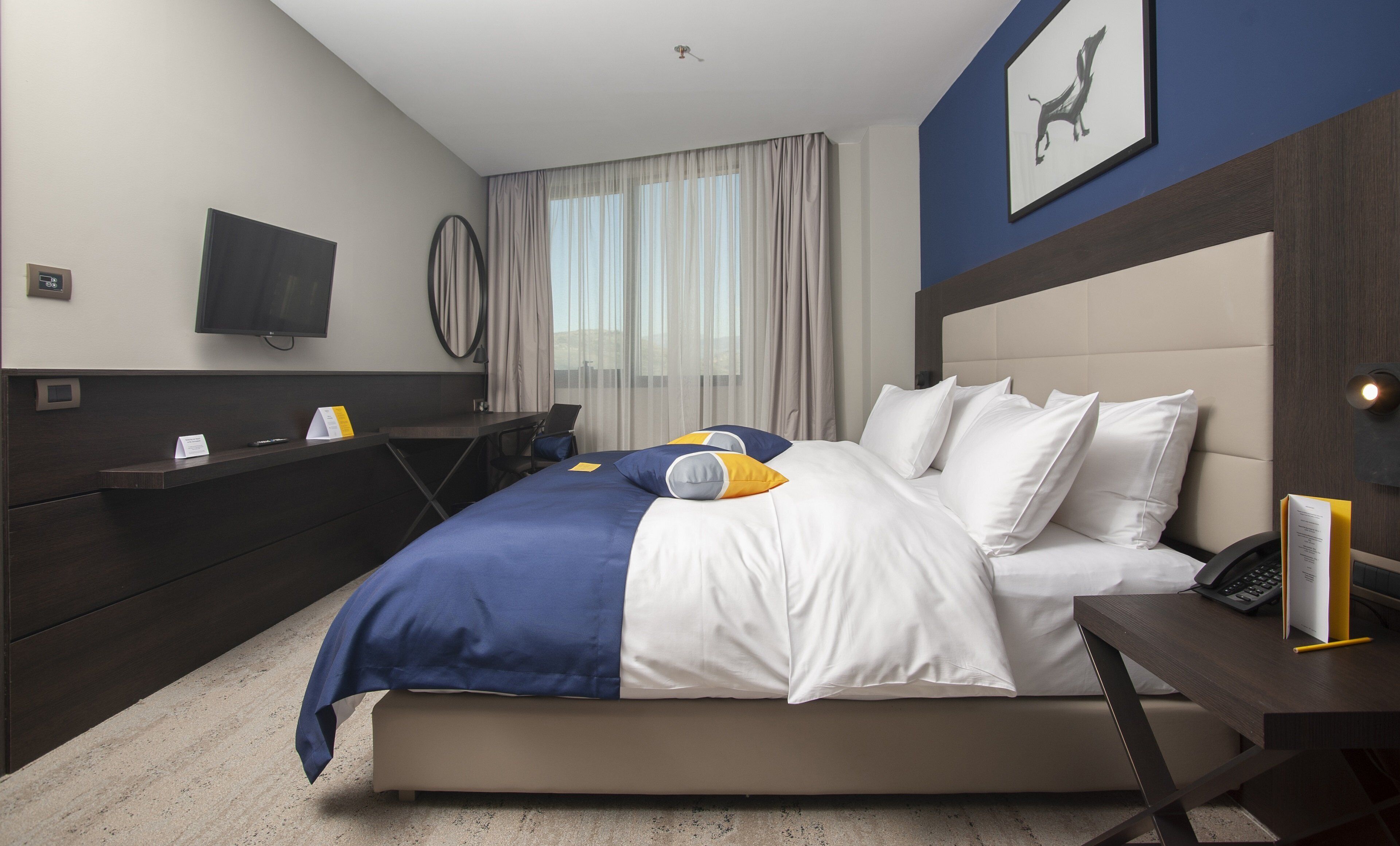A hotel room with a bed, a desk, a chair, a TV, and a window with curtains.