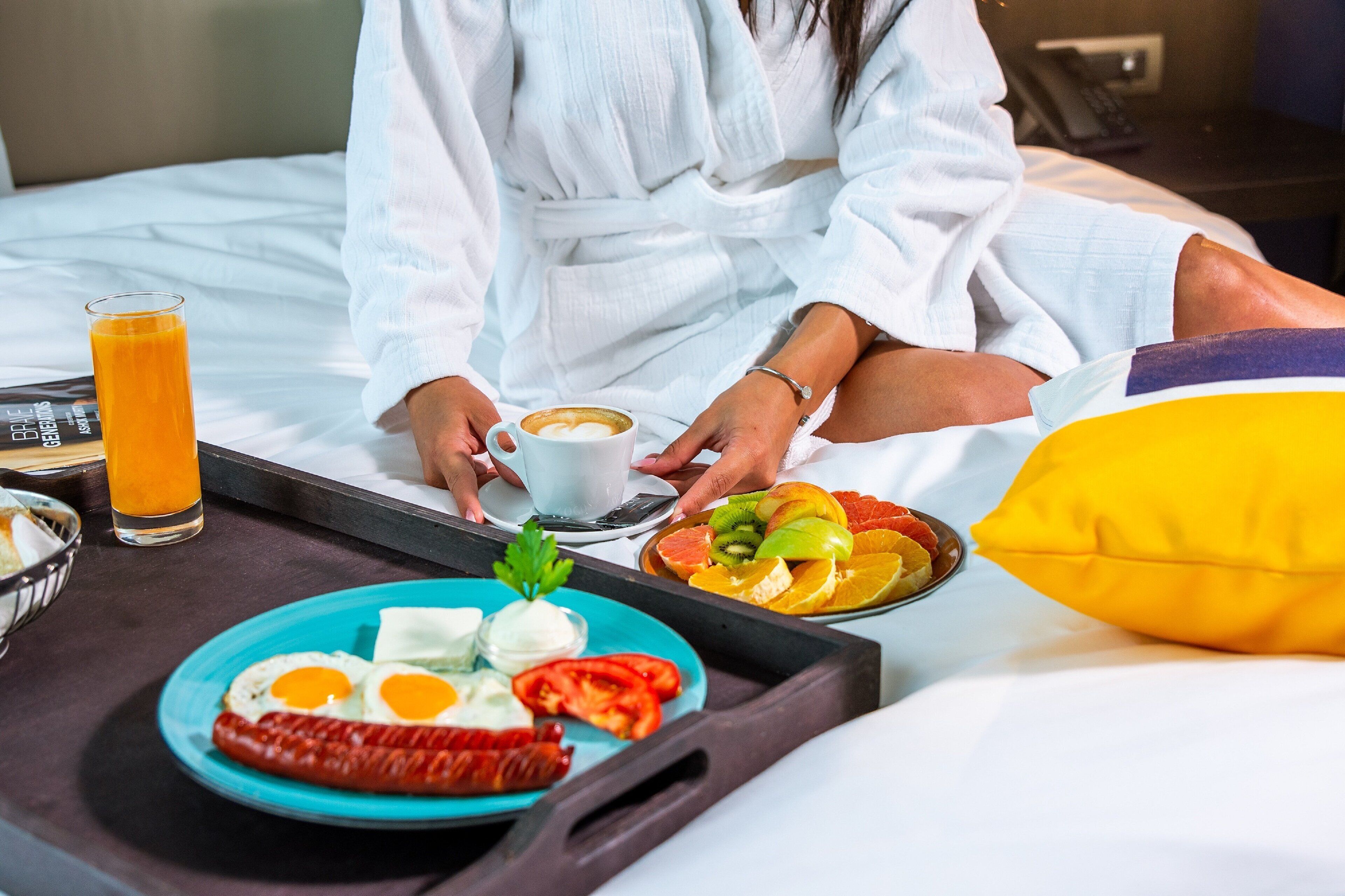 Quarto de hotel com uma cama, um tabuleiro com itens de café da manhã e uma mesinha de cabeceira com um copo de suco de laranja e uma xícara de café.