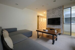 A modern living room with a sofa, a wooden coffee table, and a flat-screen TV mounted on the wall. - 4B4b Three Suites 1 Min to Blue Line MRT (Taipei)