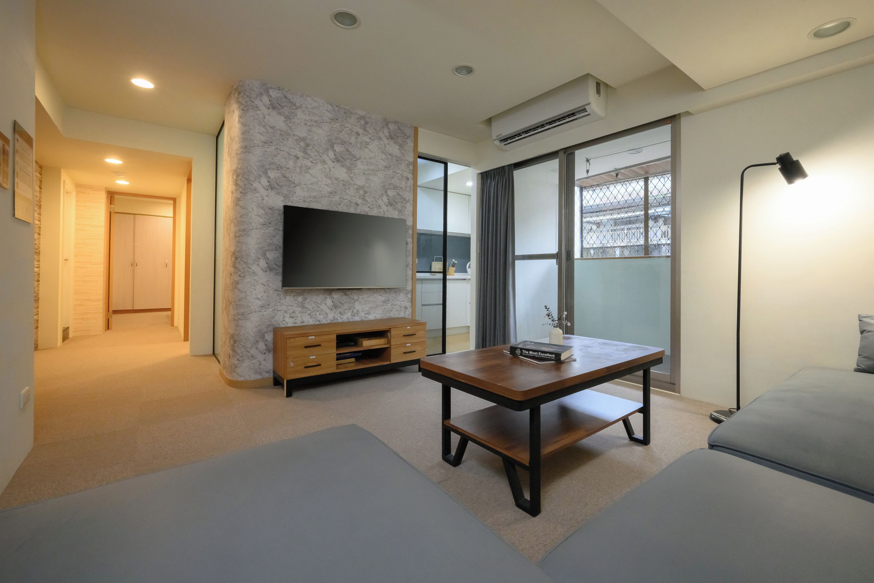 A modern living room with a marble accent wall, a flat-screen TV, a wooden entertainment unit, a sofa, and a floor lamp.