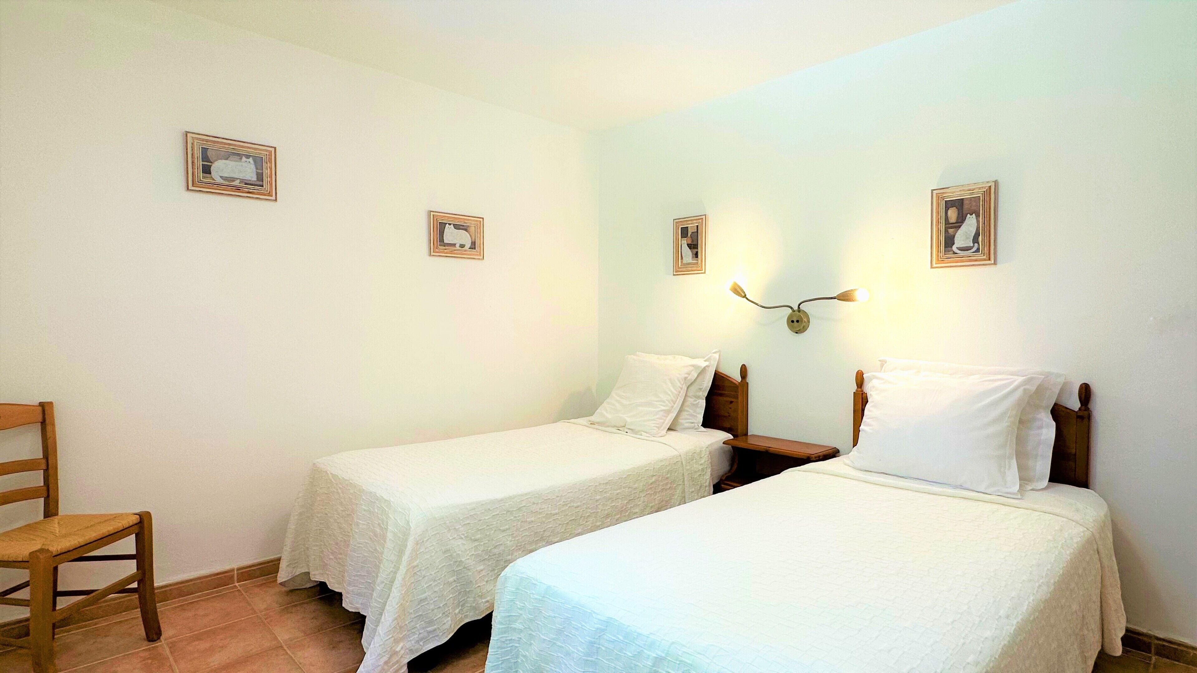 A room with two single beds, a wooden chair, and a wall-mounted lamp.