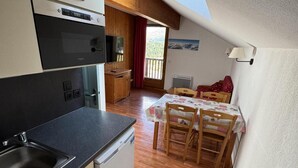 A compact kitchen with a built-in oven, a sink, and a compact refrigerator. There is a dining area with a table and chairs, and a window offering a view of the outdoors.