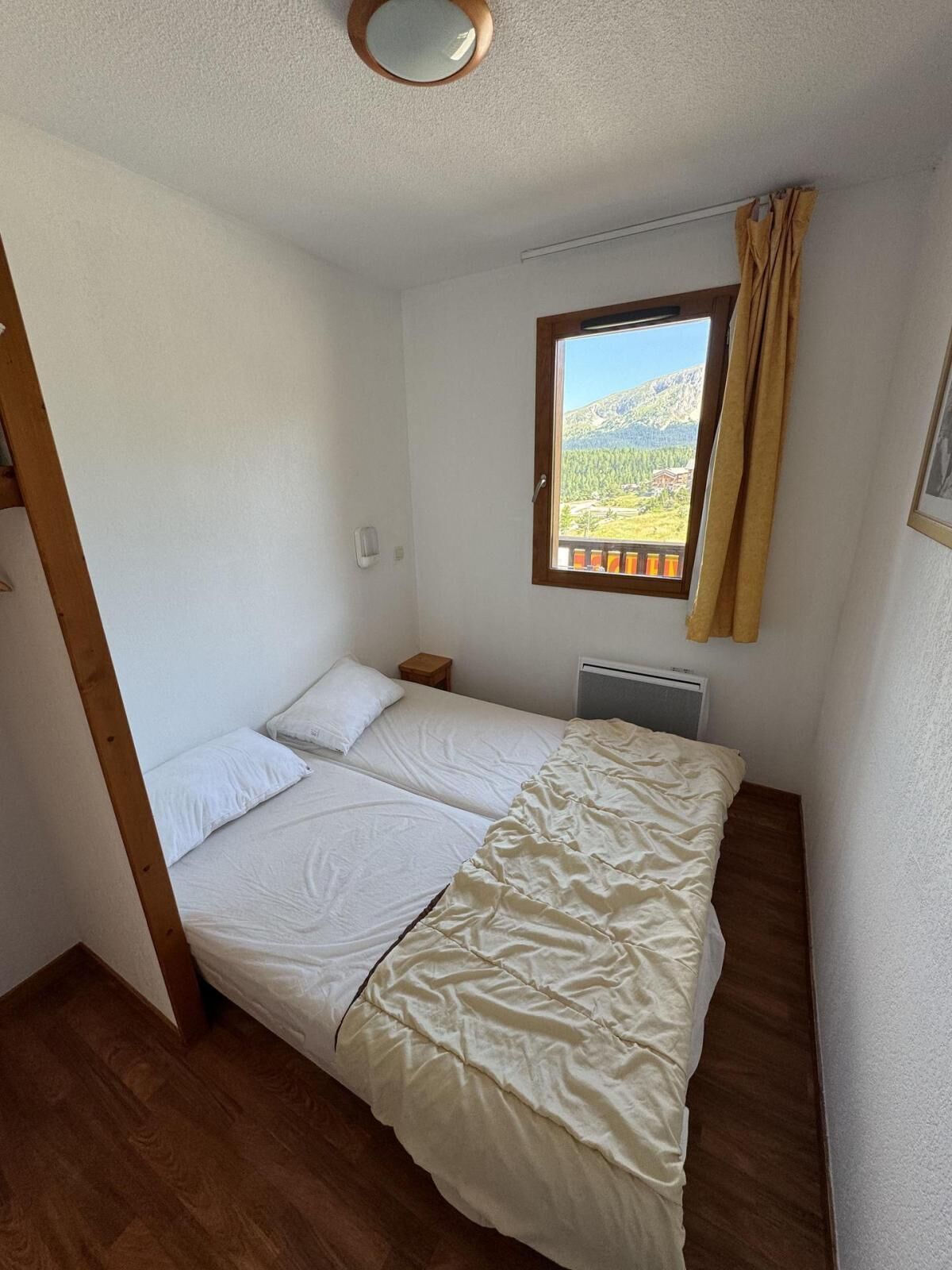 A small, single-bed room with a wooden floor, a window with a view of mountains, and a radiator.