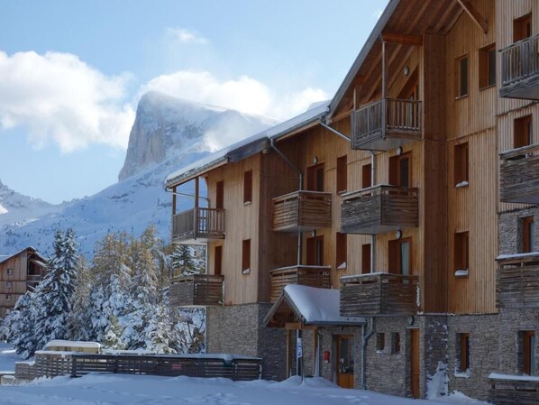 A multi-story wooden building with balconies, set against a snowy mountain backdrop.