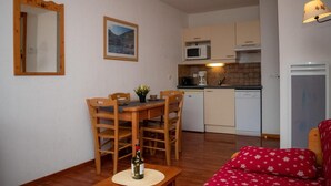 Ett kompakt bostadsutrymme med en matplats, ett litet kök och en röd soffa.