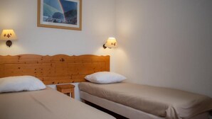 Ett rum med två separata sängar, en sänggavel i trä, sänglampor och en inramad tavla på väggen.