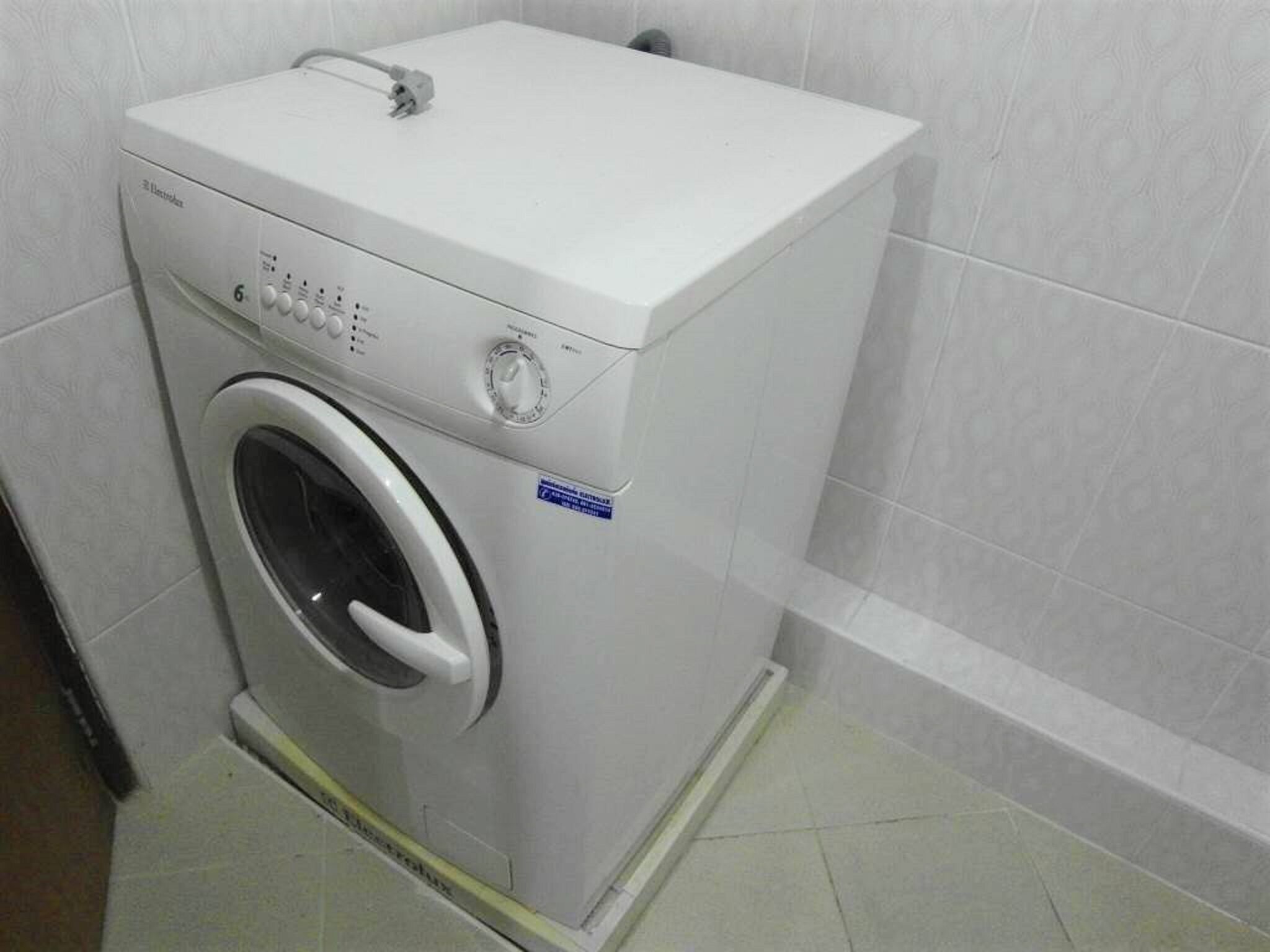 Une machine à laver à chargement frontal dans une salle de bain dont les murs et le sol sont recouverts de carreaux.