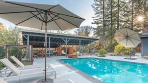 A pool area with lounge chairs, umbrellas, and a covered seating area.