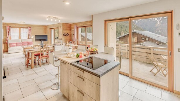 A modern kitchen with a large island, wooden cabinets, and a sliding glass door leading to an outdoor patio. - Chalet, terrace, fireplace or stove, parking, tv, ski locker, 160m², Champagny-en-Vanoise (Champagny-en-Vanoise)