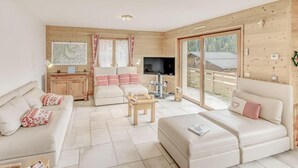 A cozy living room with a sofa, a coffee table, and a TV. There is a wooden wall and a window with curtains. - Chalet, terrace, fireplace or stove, parking, tv, ski locker, 160m², Champagny-en-Vanoise (Champagny-en-Vanoise)
