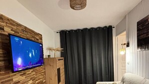 Un soggiorno con televisione montata su una parete in legno, un tavolino da caffè in legno, un divano con un cuscino decorativo e una tenda scura.
