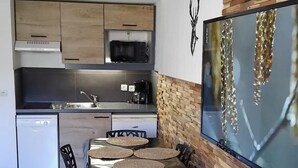 Una cucina compatta con mobili in legno, un forno a microonde e una macchina da caffè. C'è una zona pranzo con tavolo e sedie, e una parete decorativa con una testa di cervo.