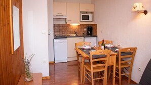Cocina compacta equipada con microondas, cafetera y lavavajillas. Cuenta con una mesa de comedor, sillas y una botella de vino.