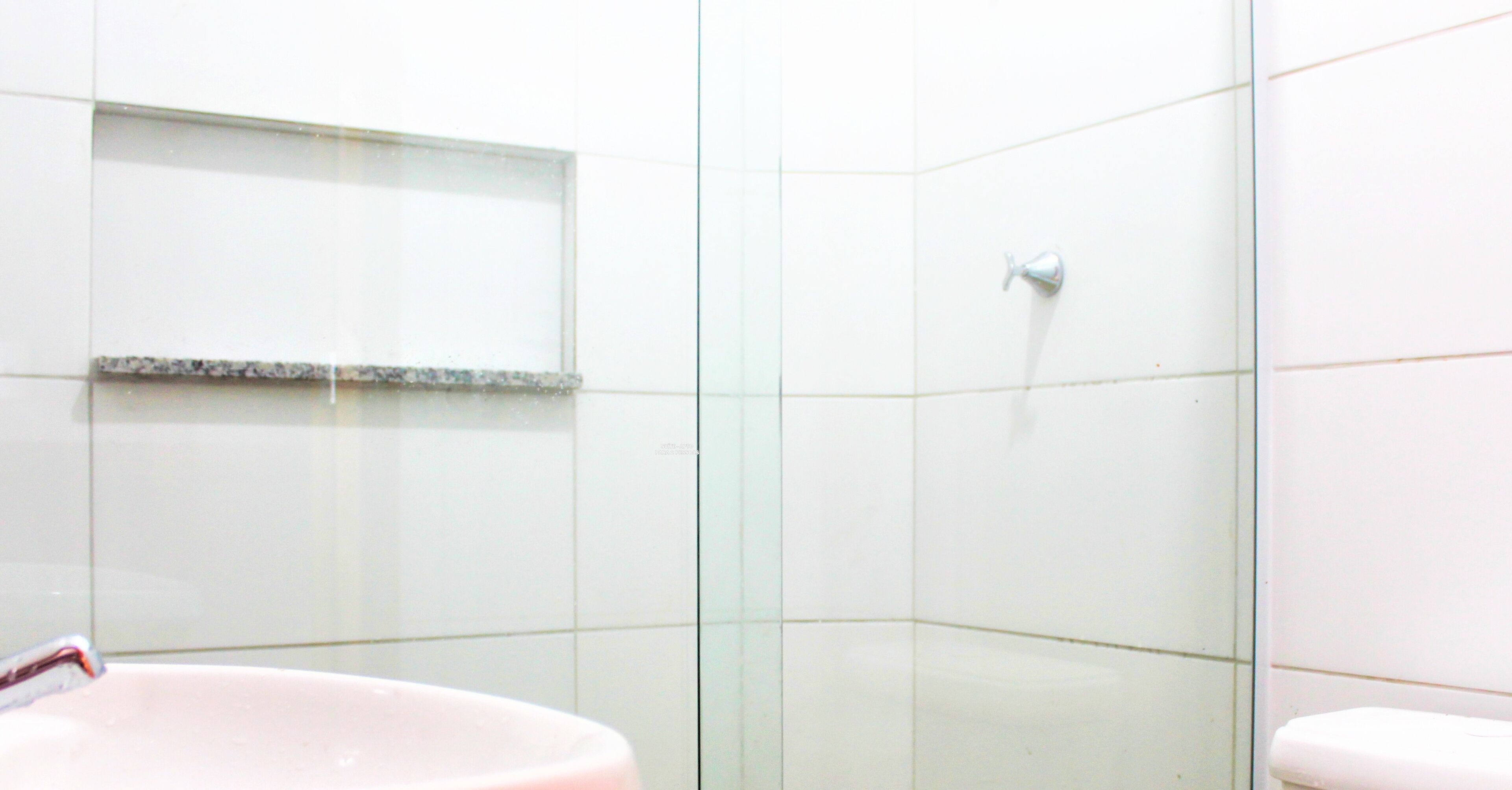 Un baño con azulejos blancos, cabina de ducha de vidrio y lavamanos blanco.