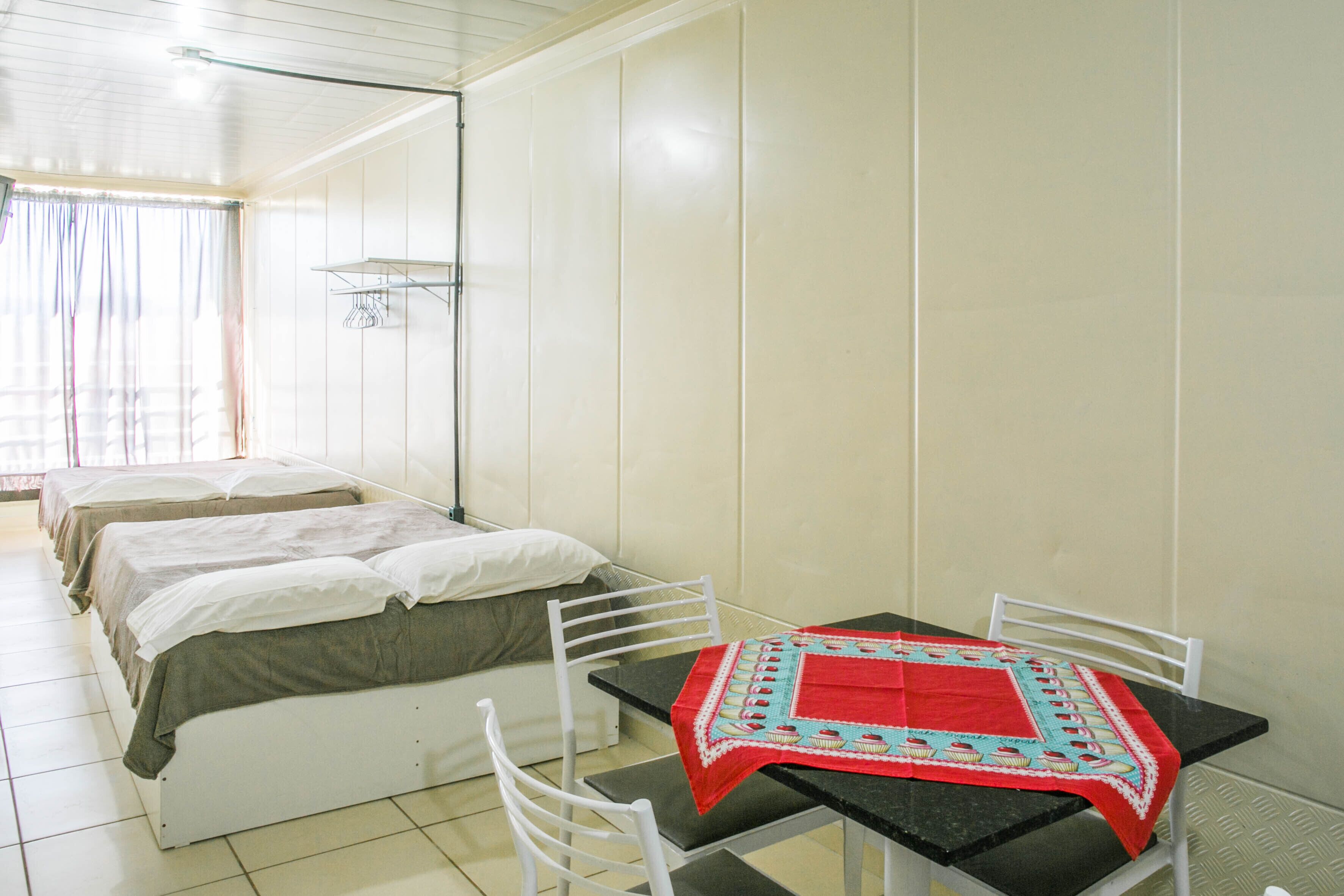 Een kamer met een bed, een tafel met een rode tafelkleed en een stoel.