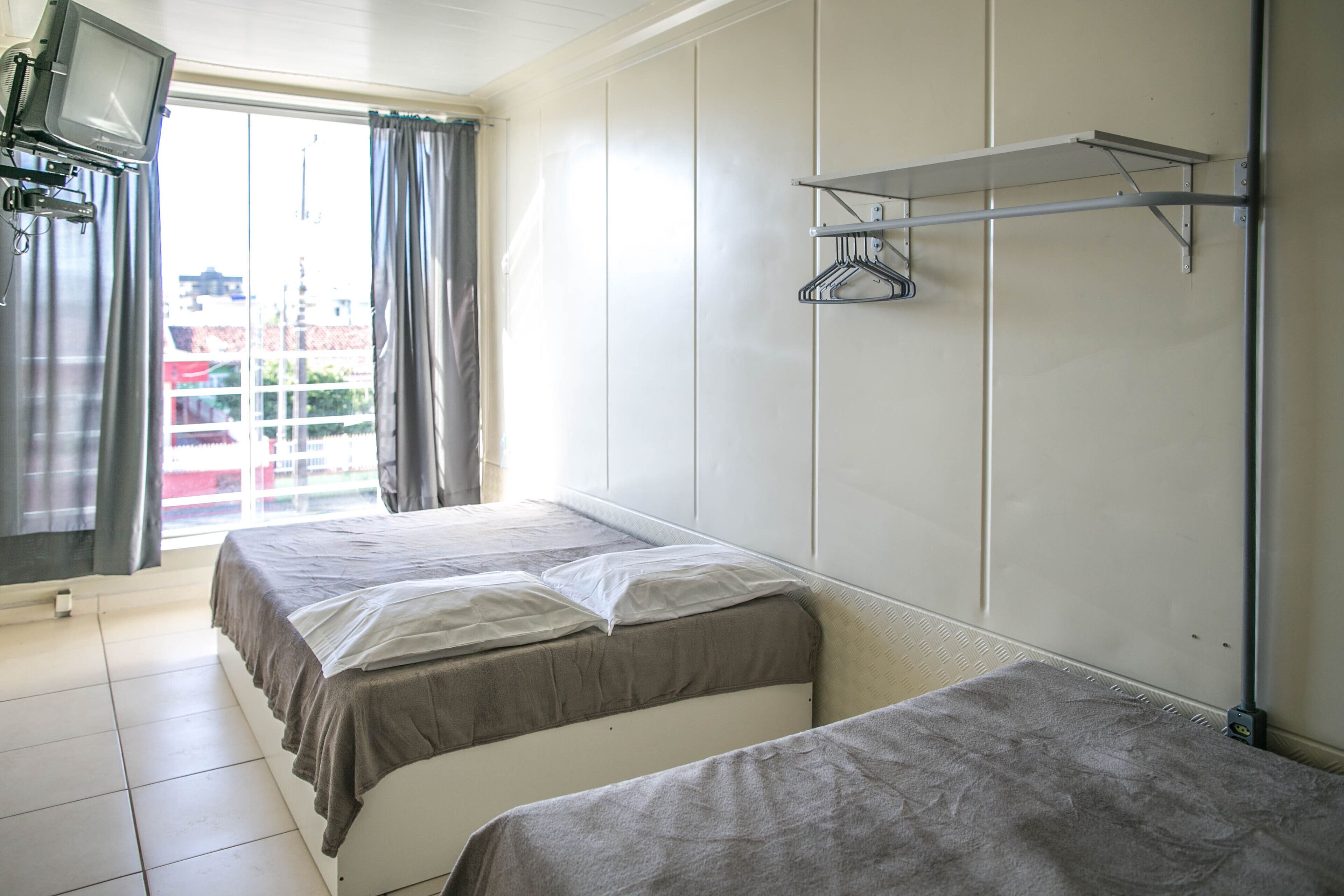 Camera d'albergo con due letti, una televisione su un supporto, uno stendibiancheria e vista esterna.