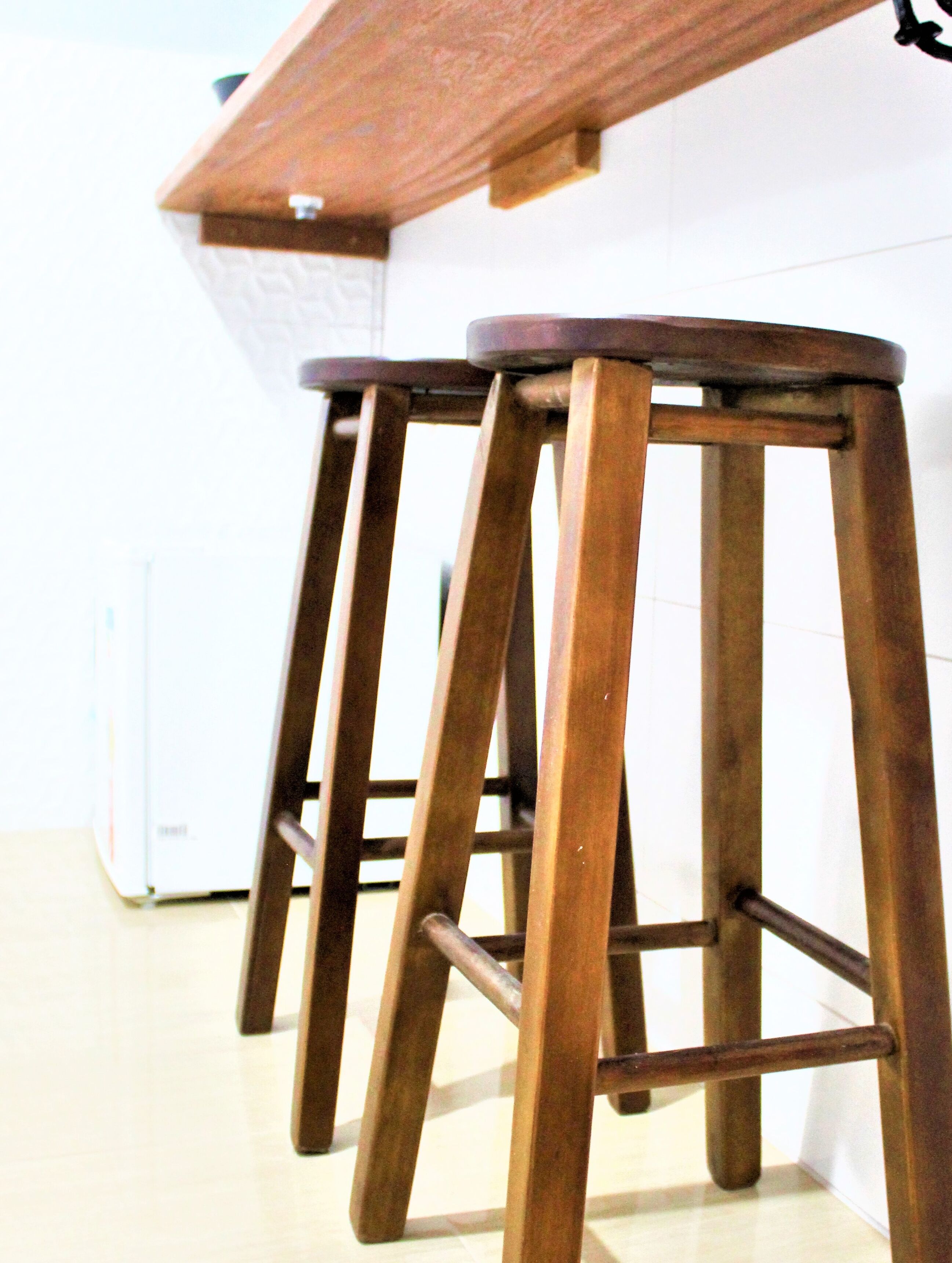 A row of wooden stools with metal legs, positioned against a white wall.