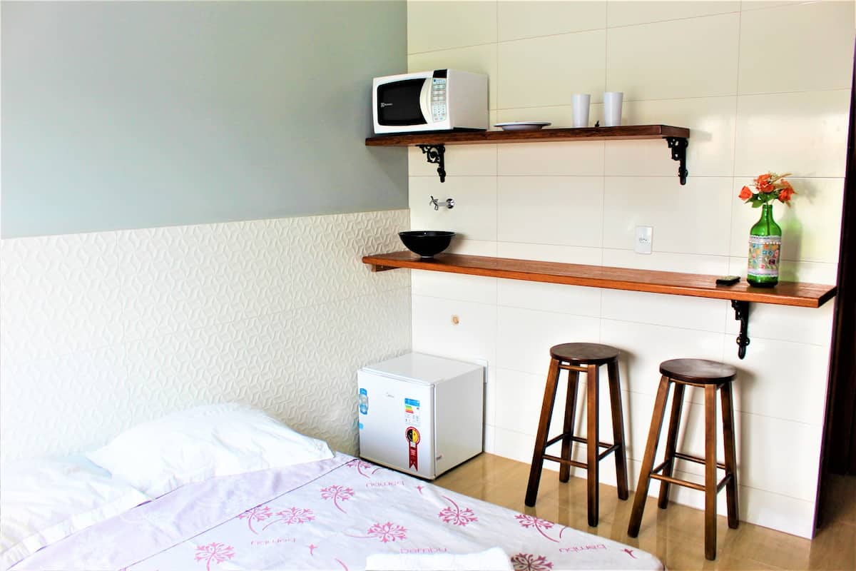 Een praktische keuken met een magnetron, een kleine koelkast en een houten bar met krukken.