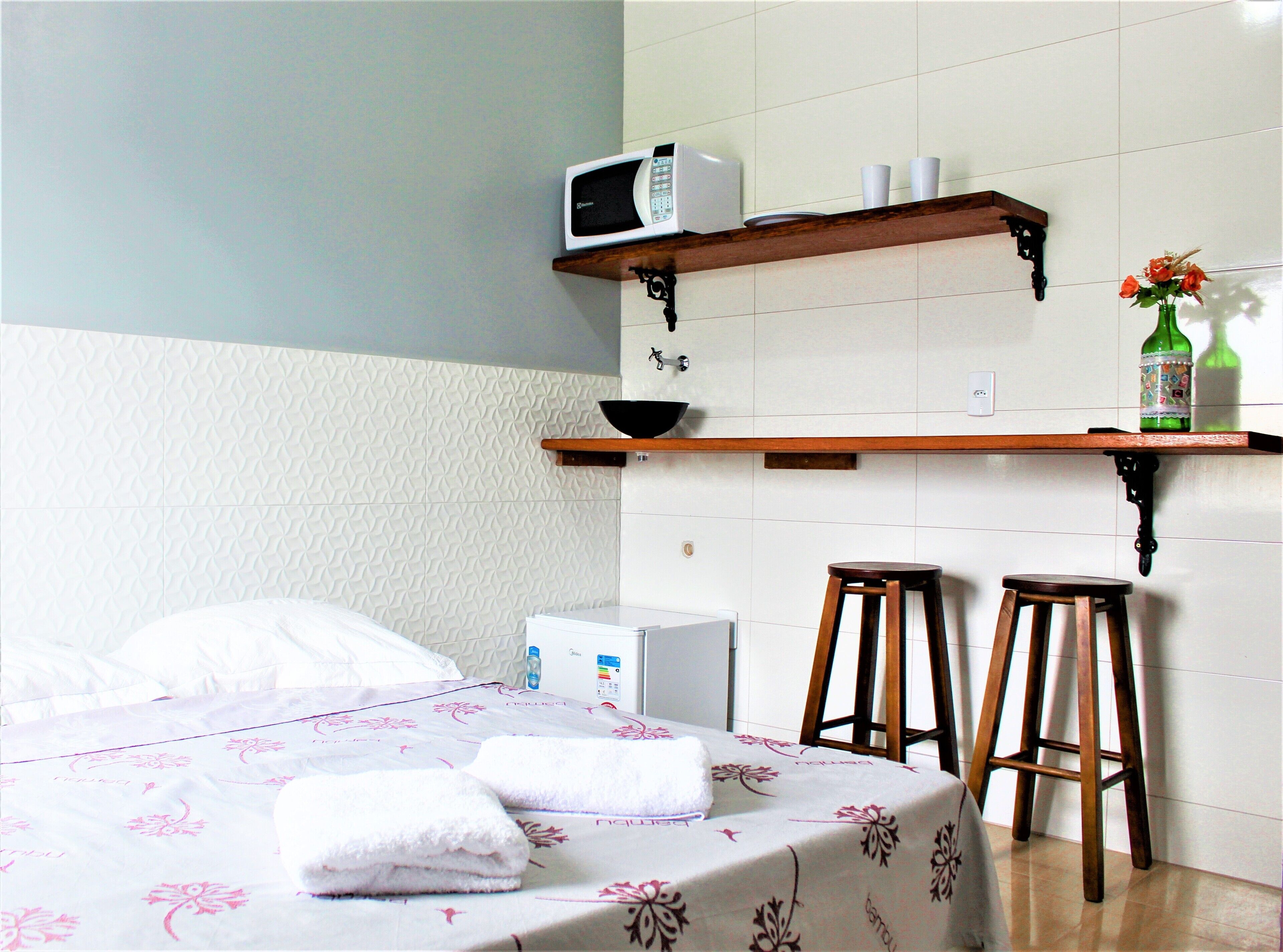 A hotel room with a bed, a small kitchenette, a sink, and two stools.